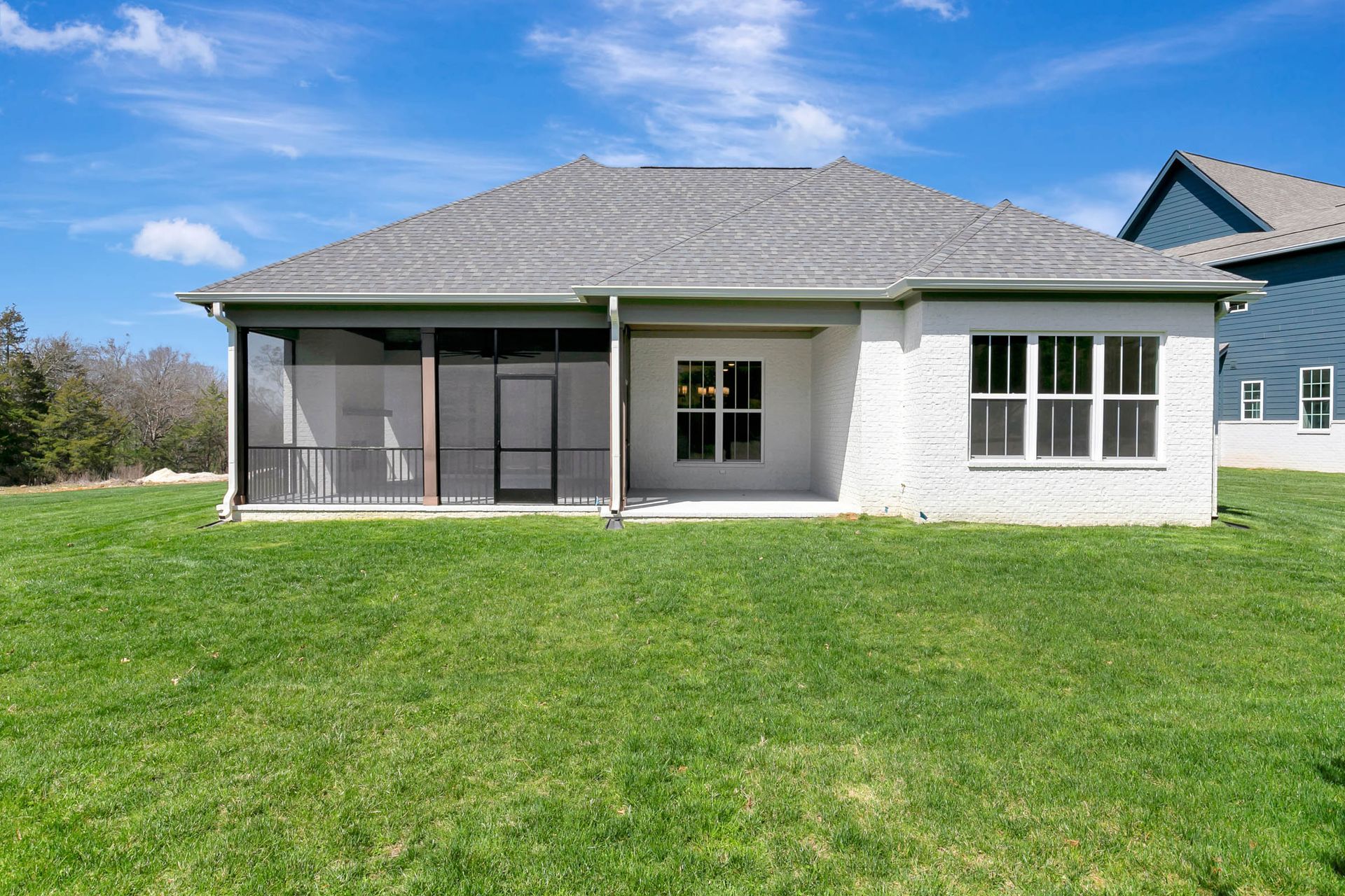 The back of a house with a screened in porch and a large lawn in front of it.