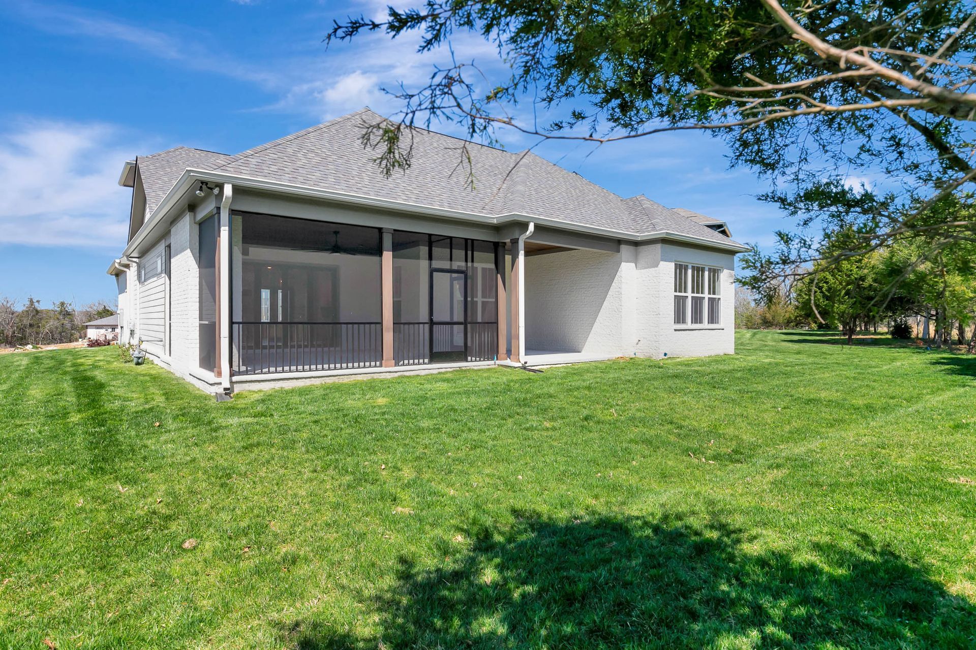 A house with a screened in porch and a large lawn in front of it.