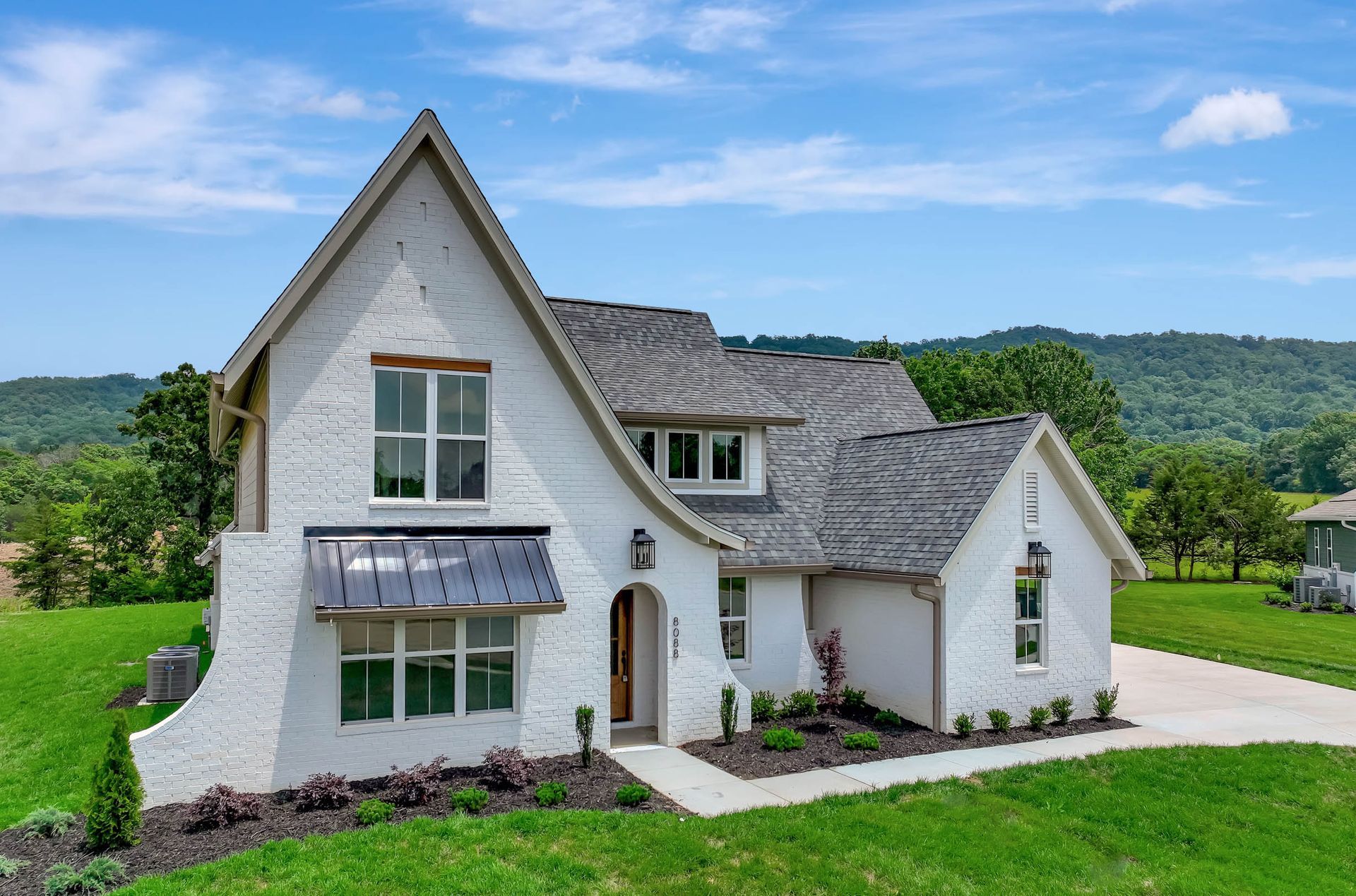 A white house with a gray roof is sitting on top of a lush green field.