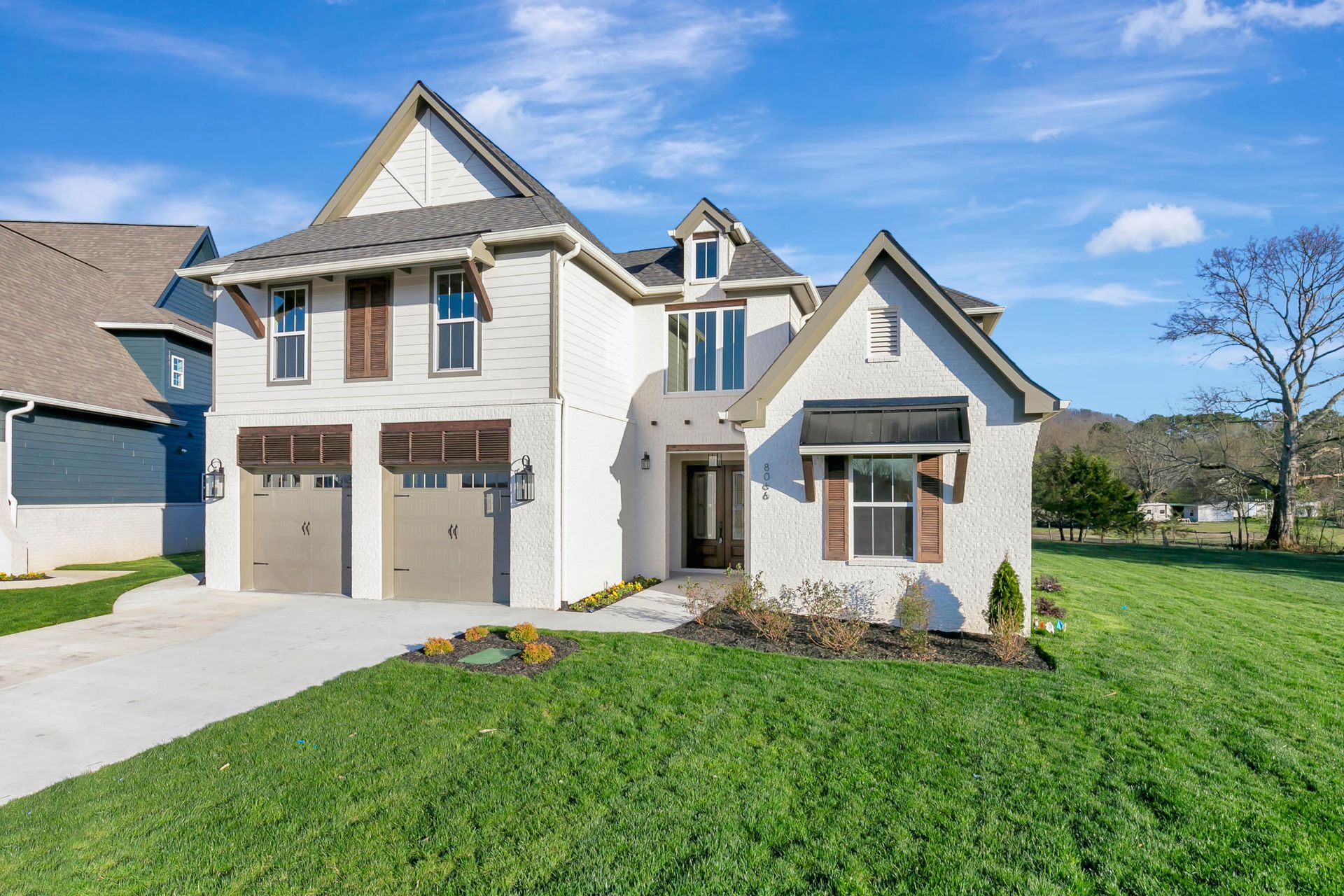 A large white house with two garages is sitting on top of a lush green field.