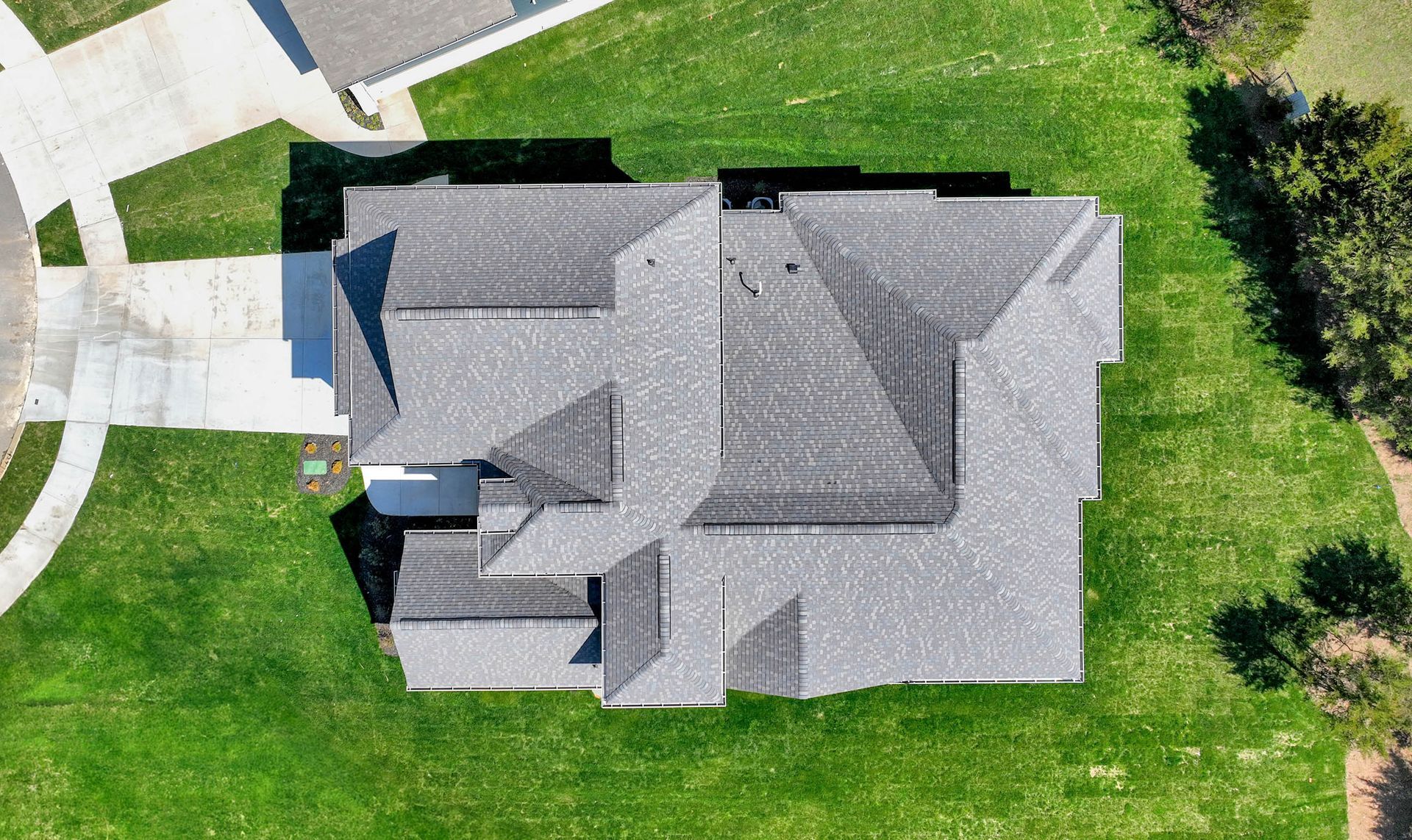 An aerial view of a house with a gray roof and a lush green lawn.