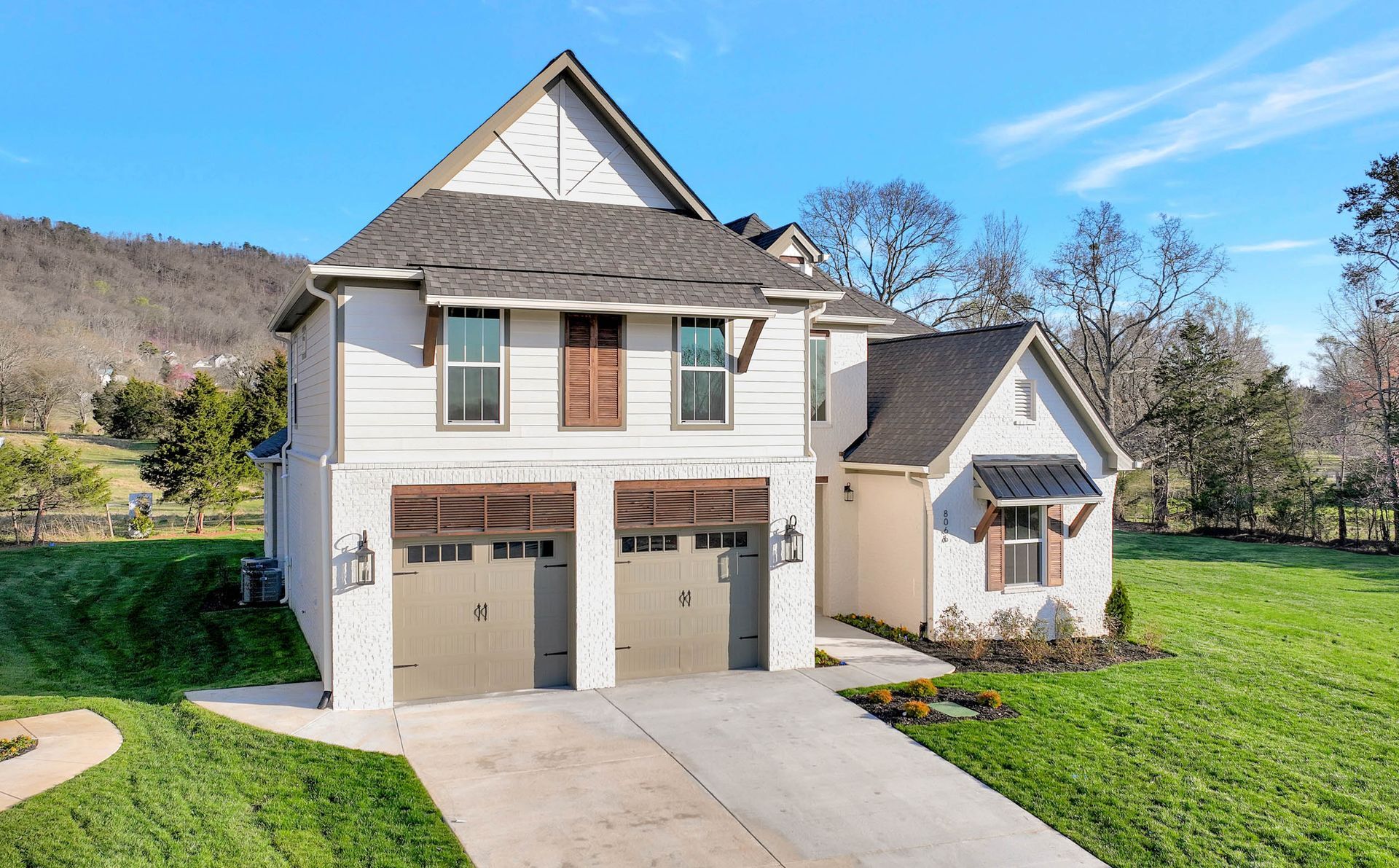 A large white house with two garage doors is sitting on top of a lush green hillside.