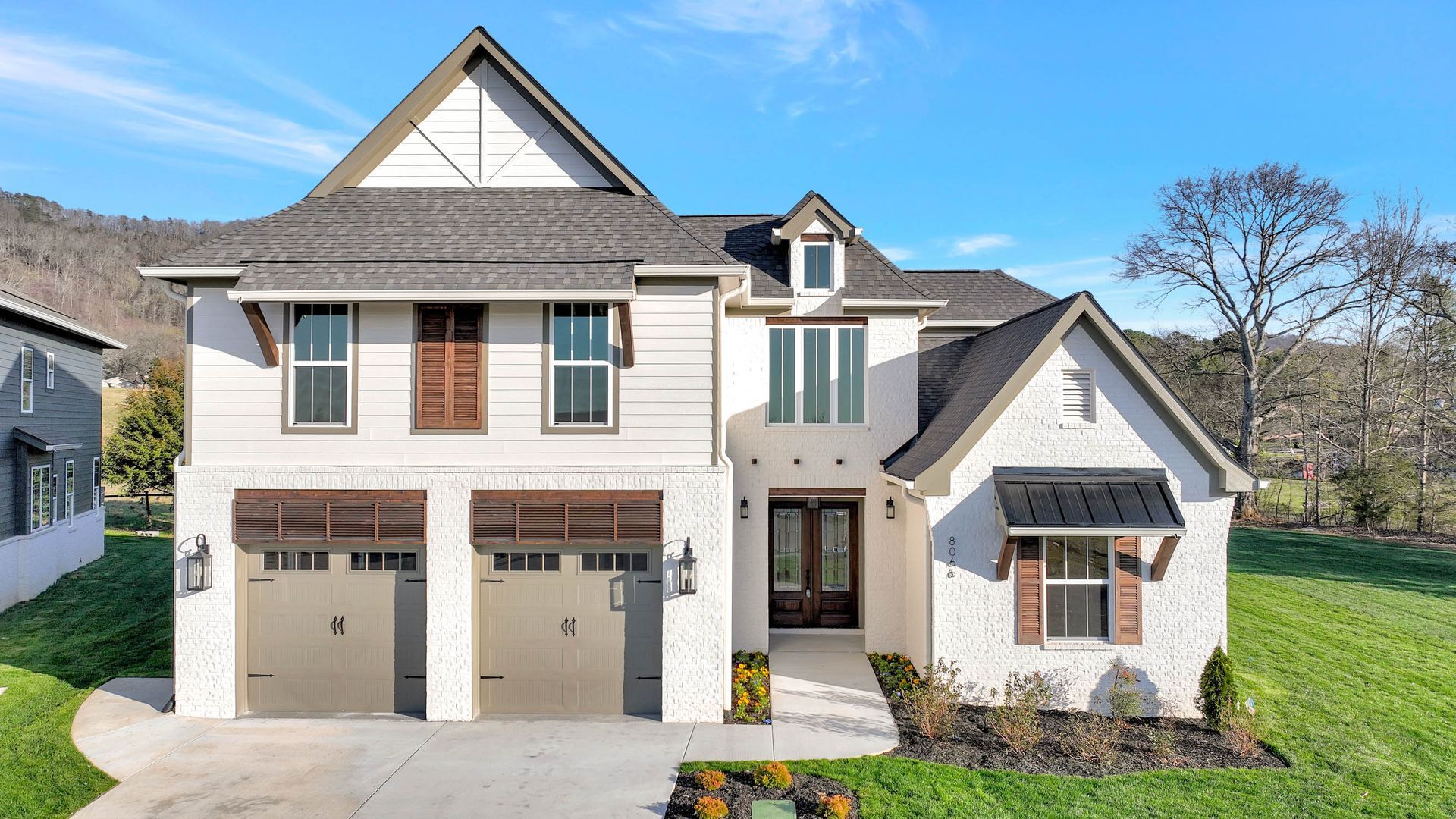 A large white house with two garages is sitting on top of a lush green hillside.