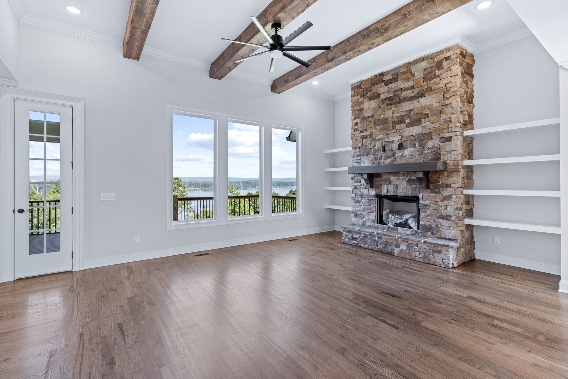 an empty living room with a stone fireplace and a ceiling fan .