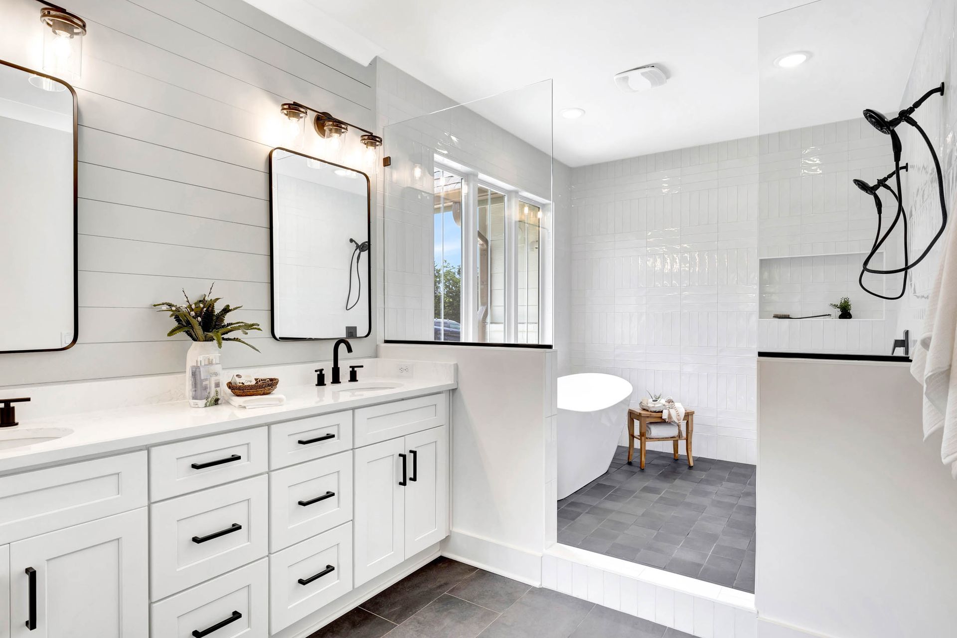 A bathroom with two sinks , two mirrors , a tub , and a walk in shower.