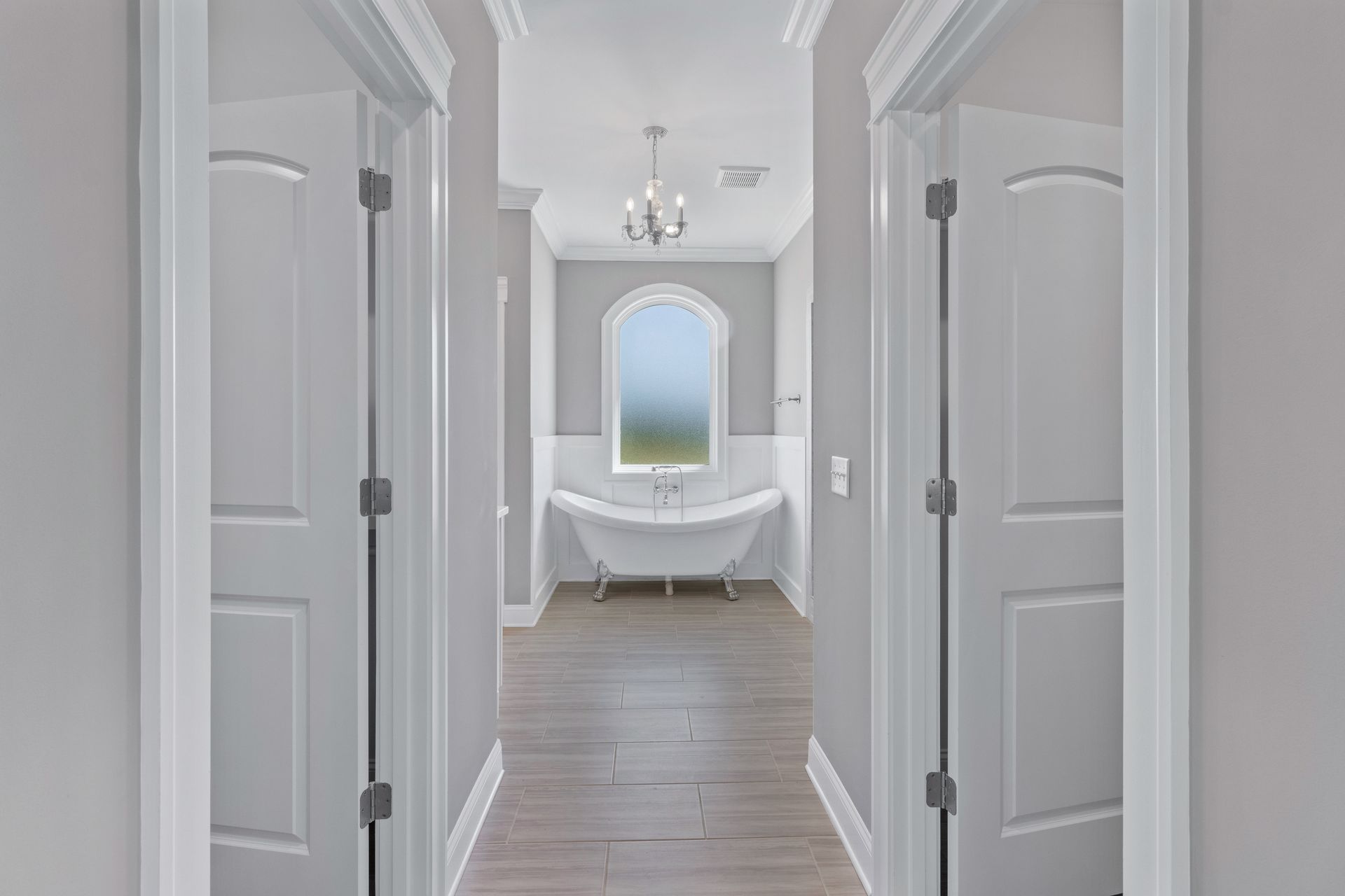 a hallway leading to a bathroom with a tub and a window .