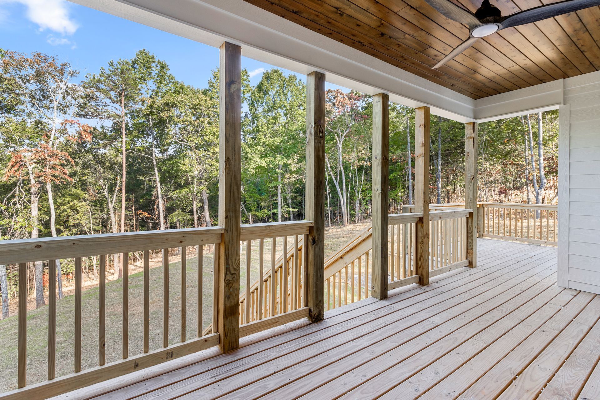 an empty screened in porch with a ceiling fan and trees in the background .