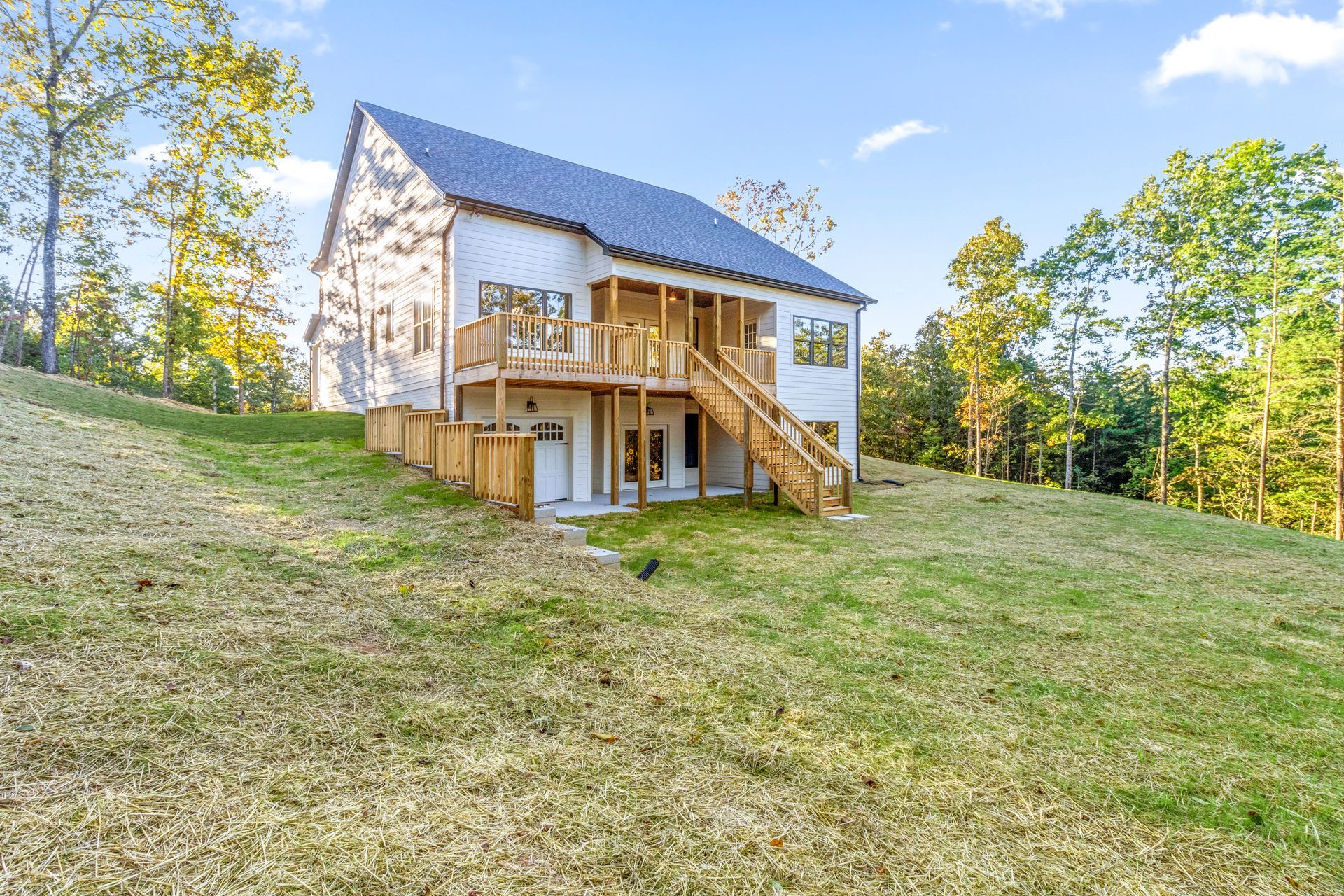 a large white house with a wooden deck is sitting on top of a grassy hill .