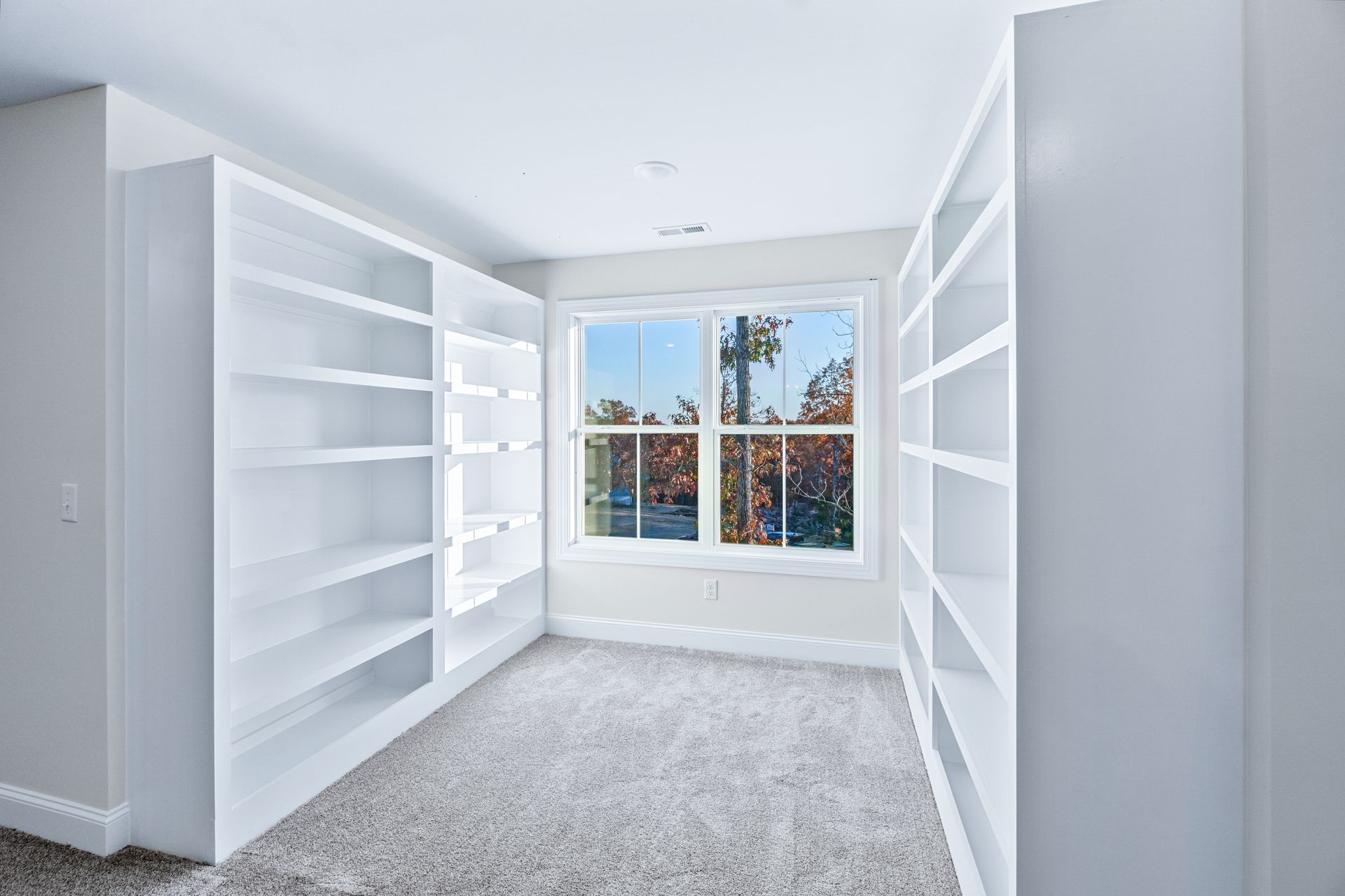 an empty room with lots of shelves and a window .