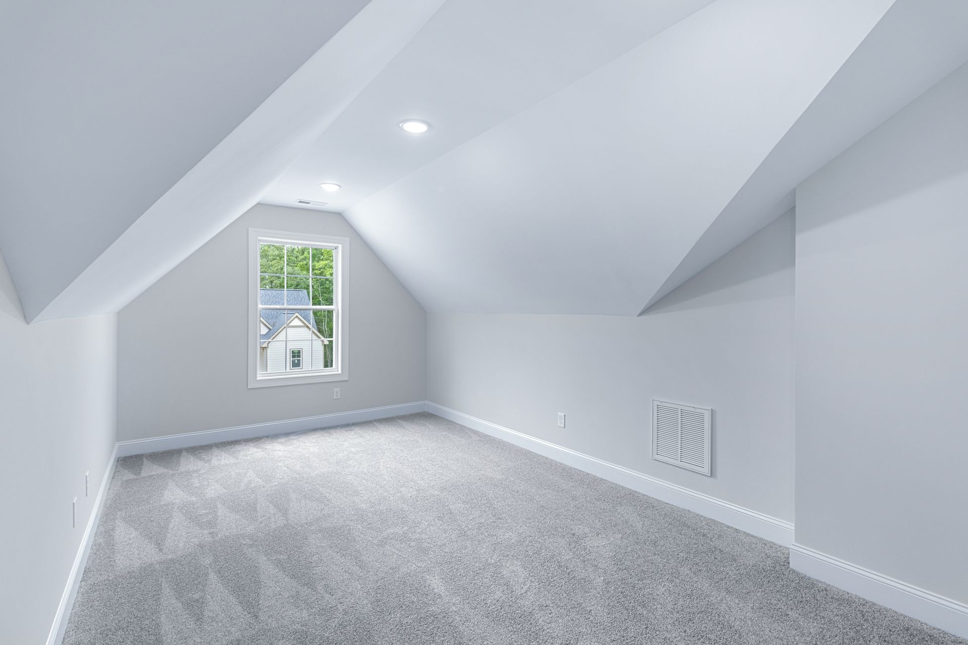 an empty attic with a window and a gray carpet .