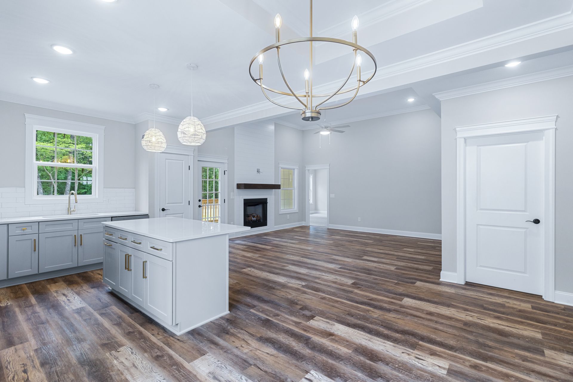 An empty kitchen with white cabinets , hardwood floors , a fireplace and a chandelier.