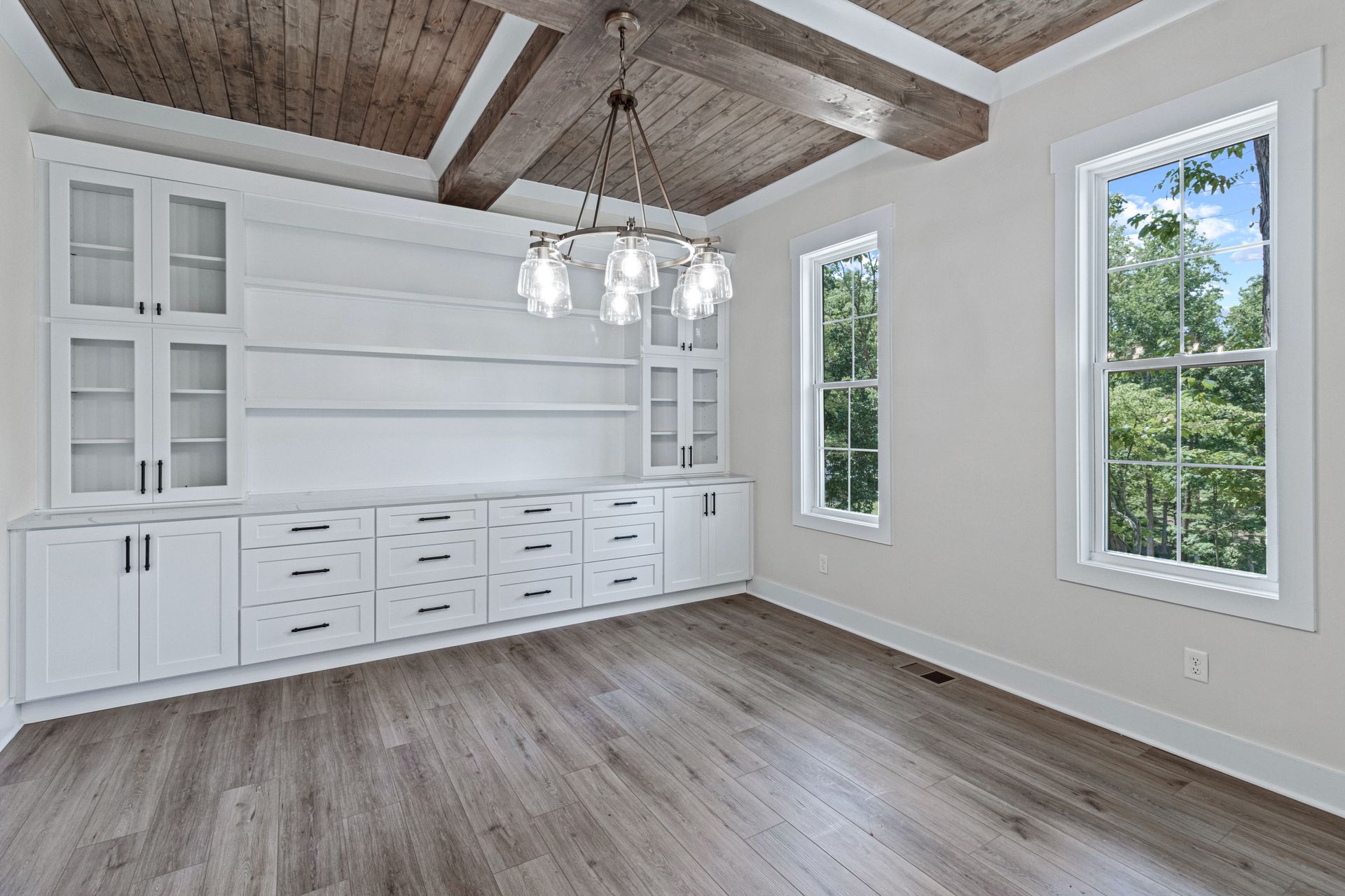 an empty room with hardwood floors , white cabinets , and a wooden ceiling .