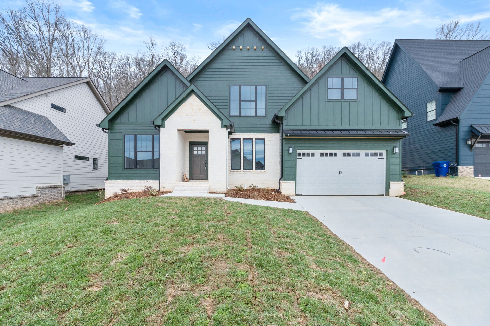 the front of a house with a green siding and a white garage door .
