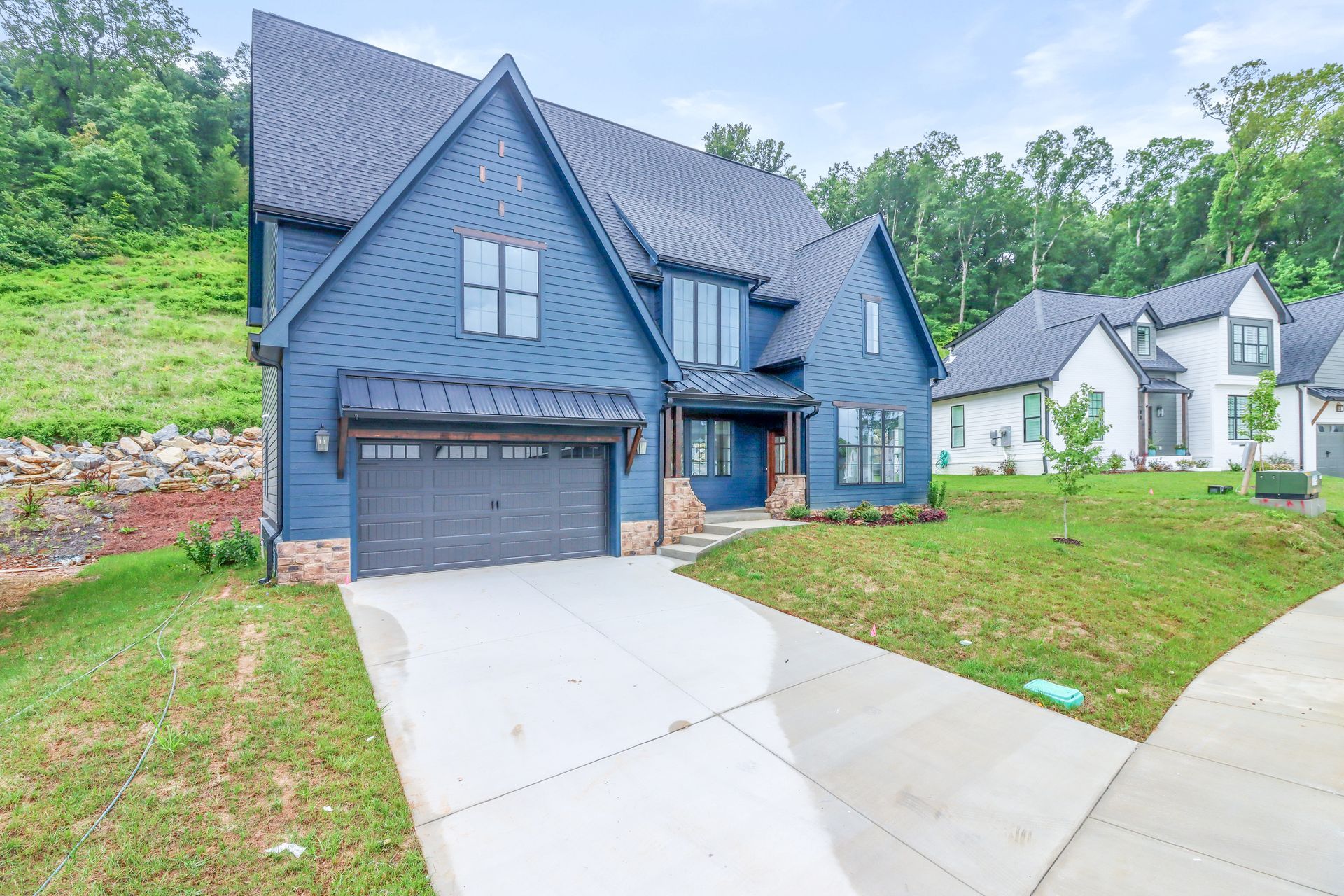 a large blue house with a black garage door is sitting on top of a lush green hillside .