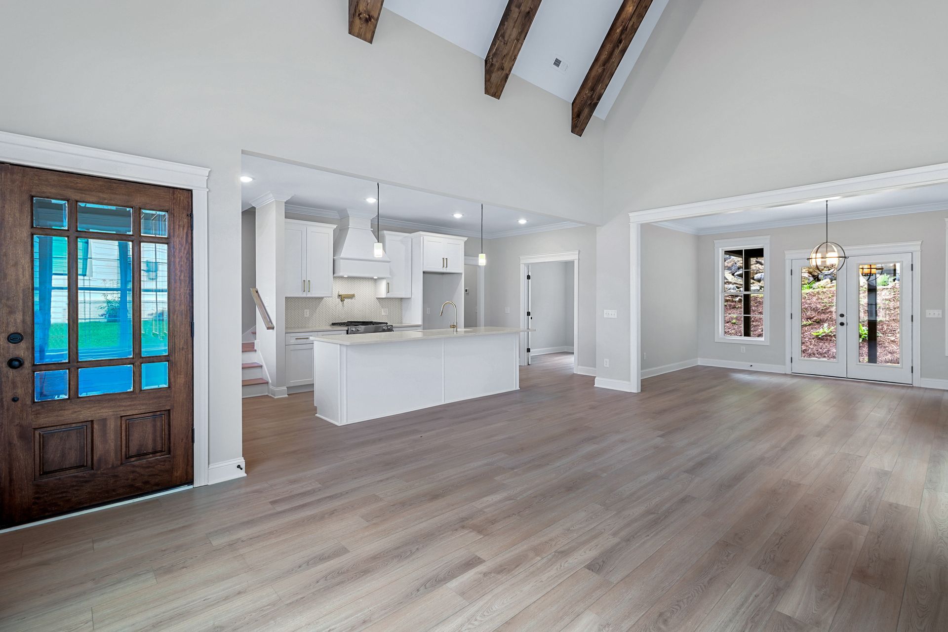 a large empty room with hardwood floors and a kitchen in the background .