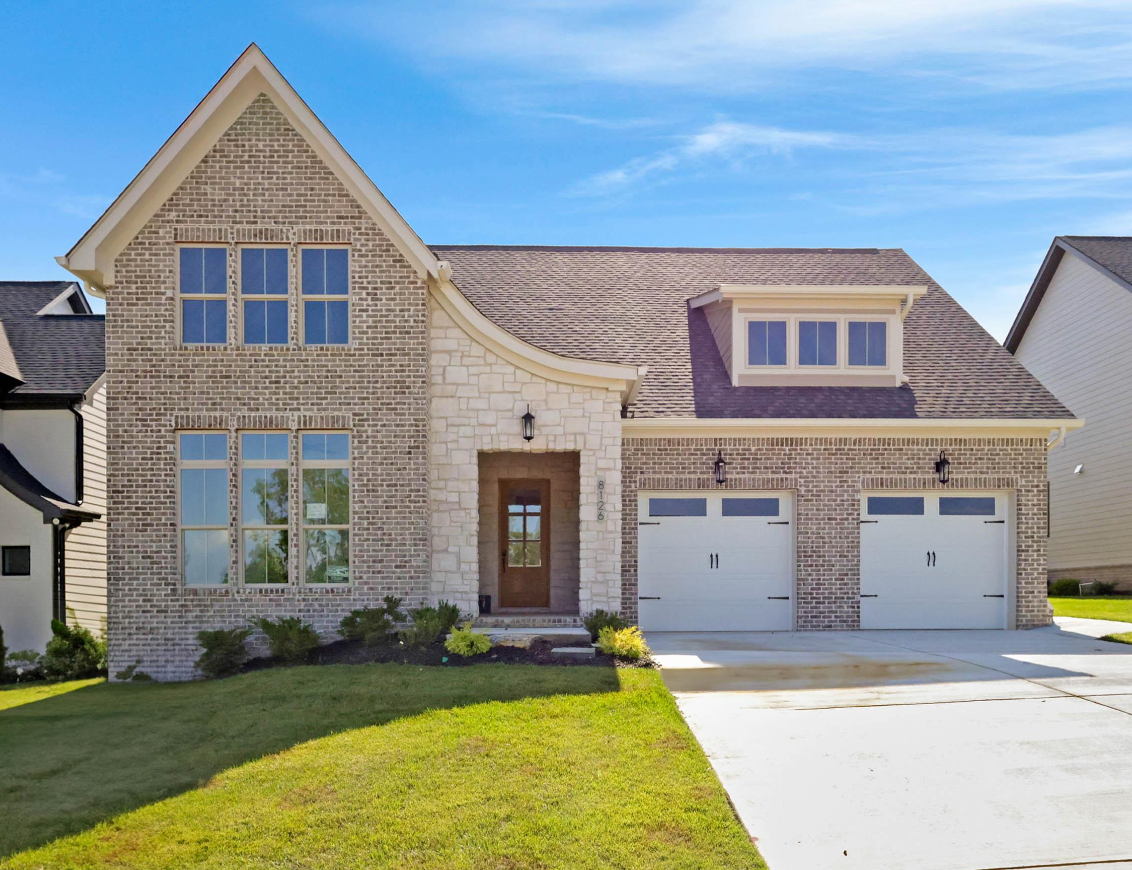 Two-story brick house with white trim, arched stone entrance, attached two-car garage, and blue sky.