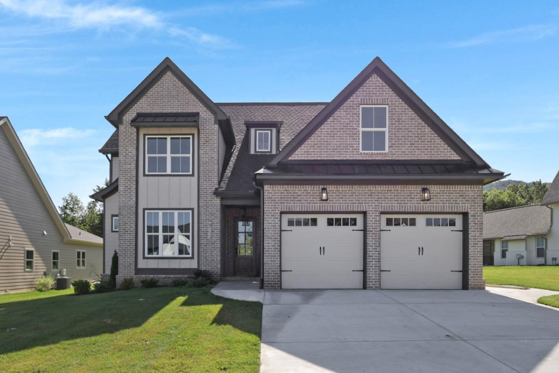 Two-story white house with light stone accents, two-car garage, and blue sky.