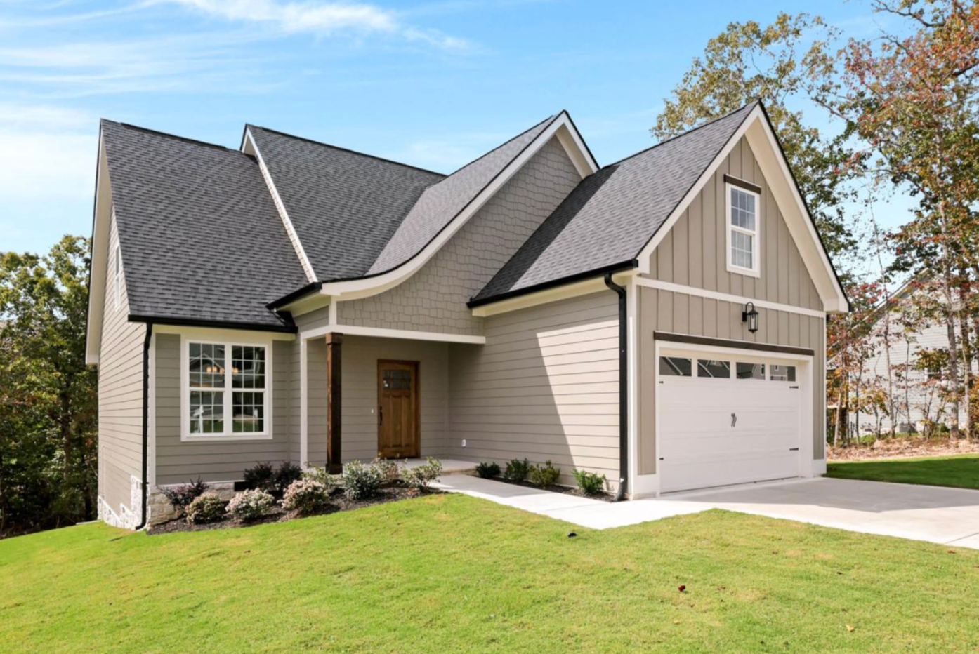 Gray house with white trim, brown door, and attached garage on a green lawn.