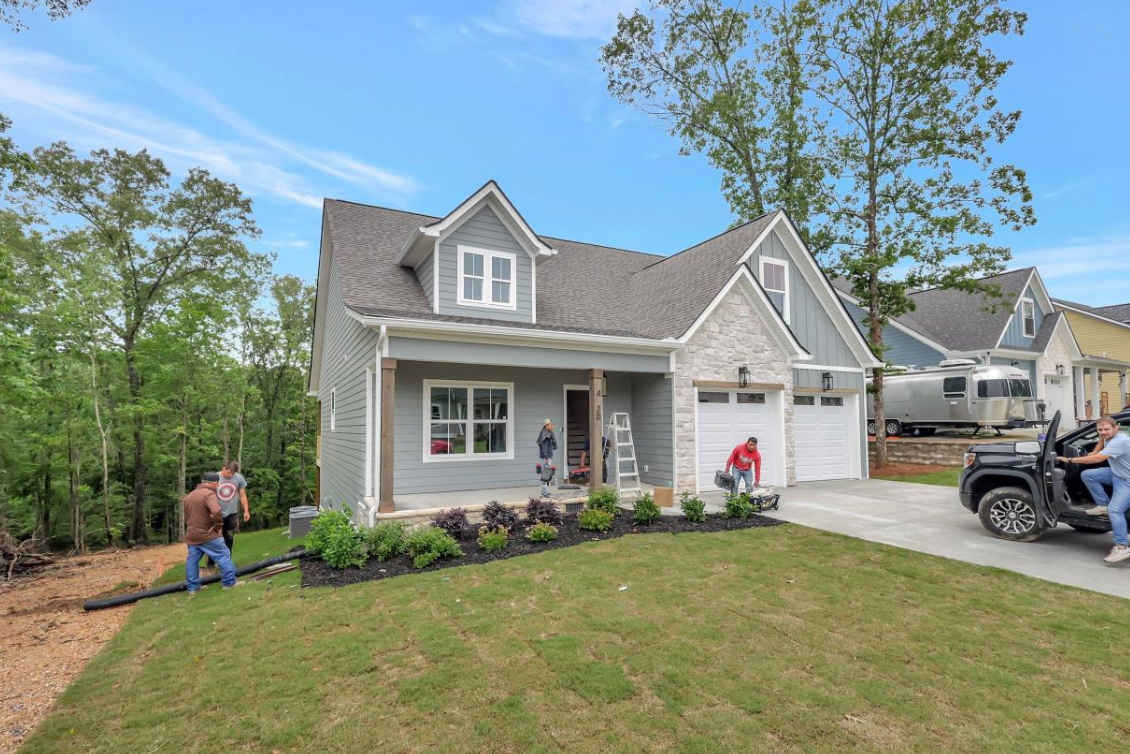 Gray house with stone accents, people working in front yard, parked vehicle.