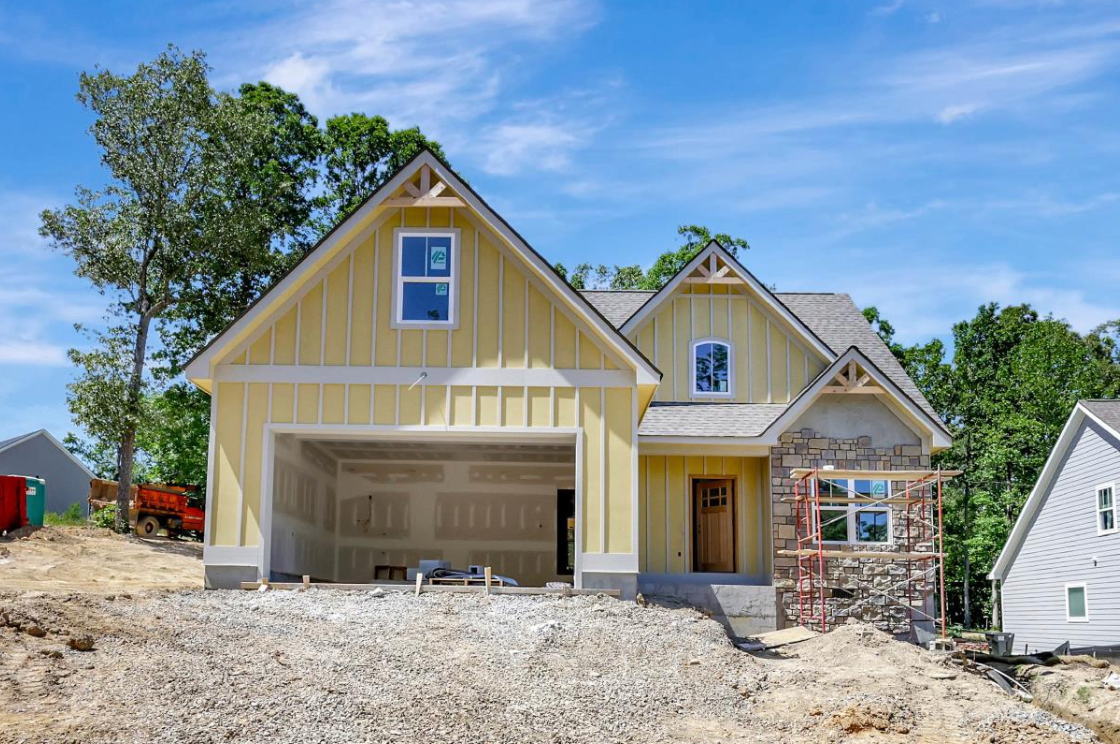 Yellow house under construction with stone accents, garage, and blue sky.
