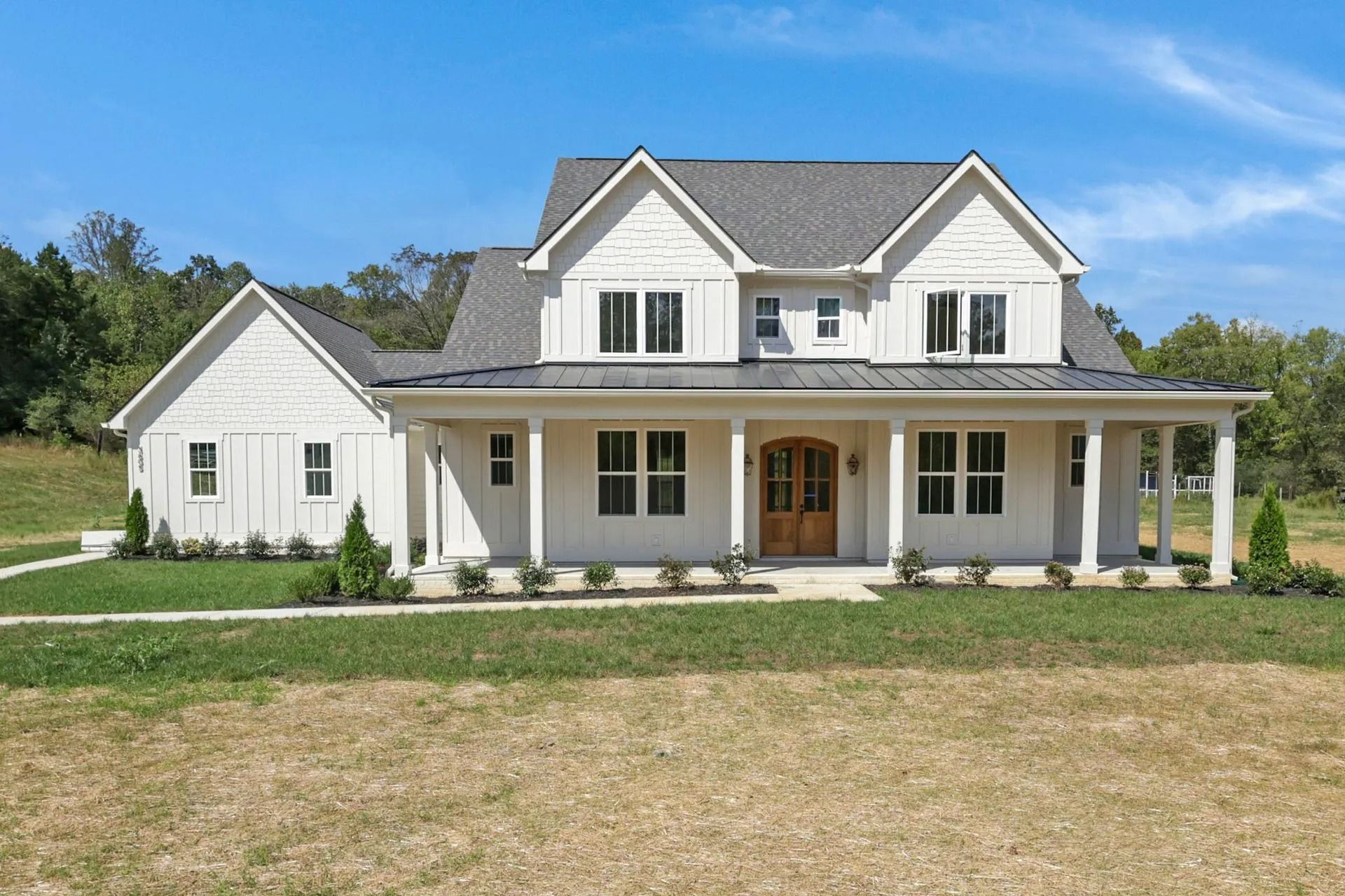 White farmhouse with black trim and a wraparound porch against a blue sky.