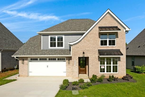 Two-story brick house with a gray roof and awnings, set on a green lawn with a white garage door.