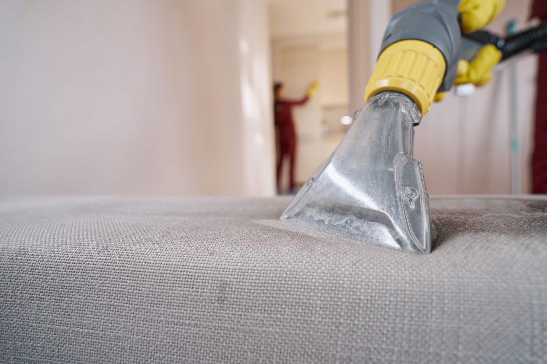 Worker vacuuming sofa using extractor nozzle.