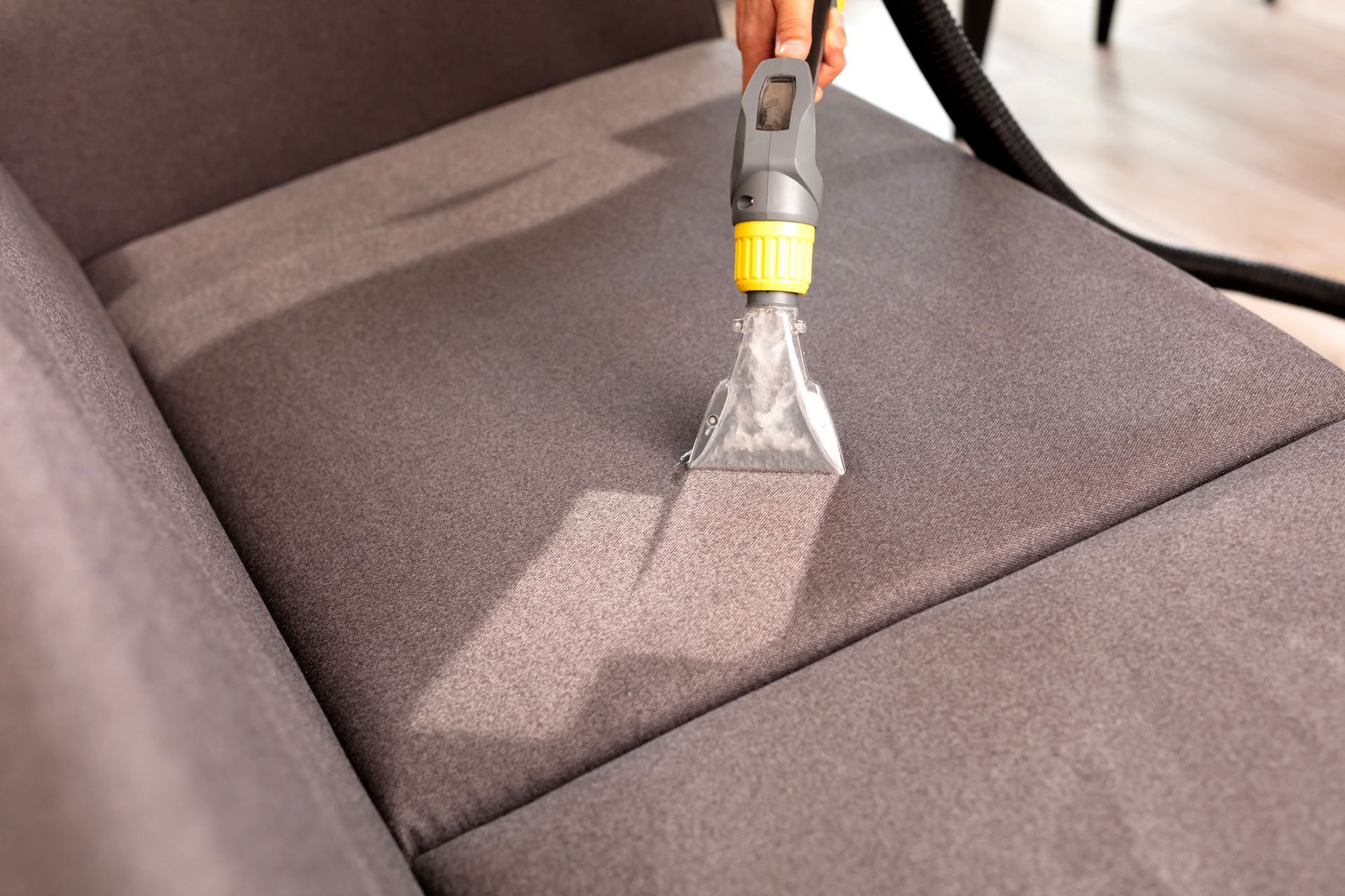 A man using a vacuum for furniture cleaning inside a home