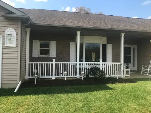 A front view of a house with a brick exterior, a white porch railing, and a white rocking chair on the porch.