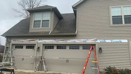 A residential garage undergoing siding and trim repairs with construction ladders placed in front of the structure.
