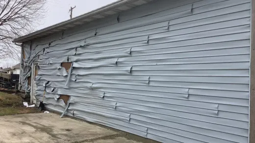 A pale blue building wall with vinyl siding that is severely melted, warped, and damaged by intense heat.