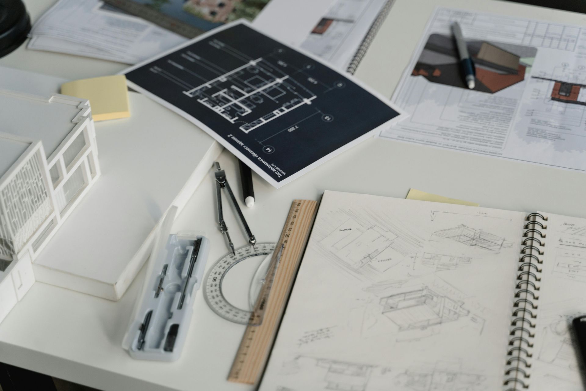 Architectural workspace with blueprint, sketchbook, ruler, and model house on a white desk