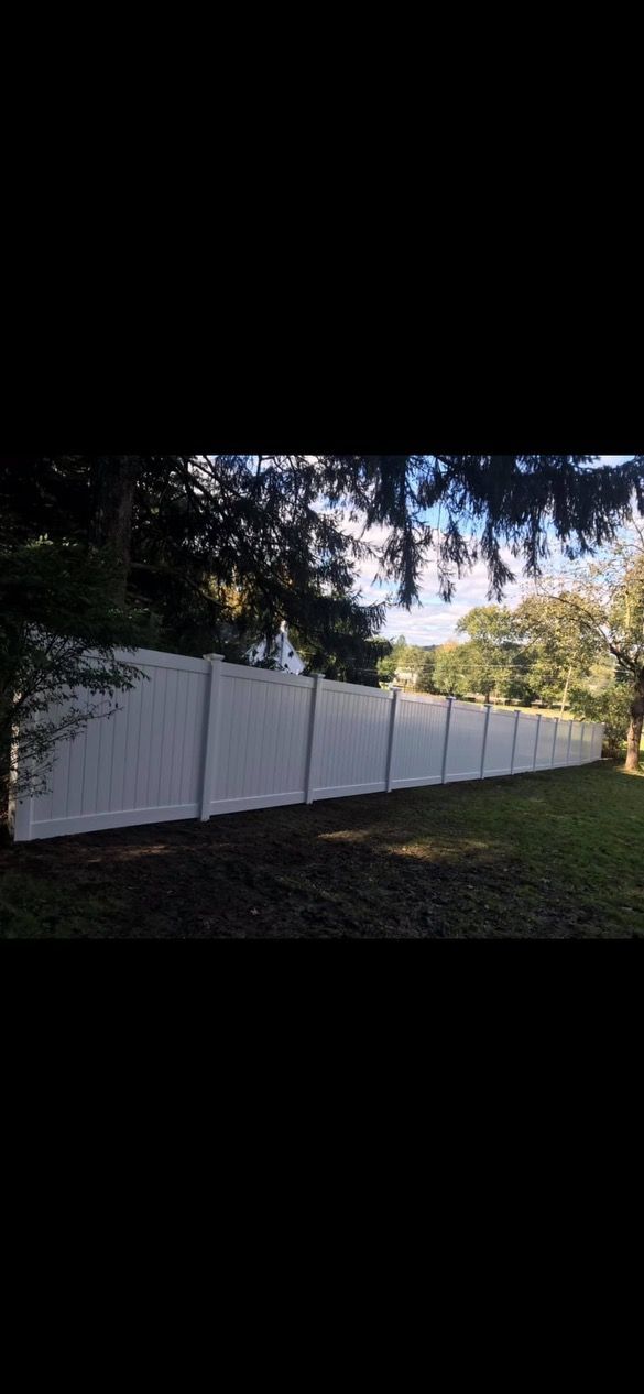 Long white fence along a grassy path beside trees at dusk