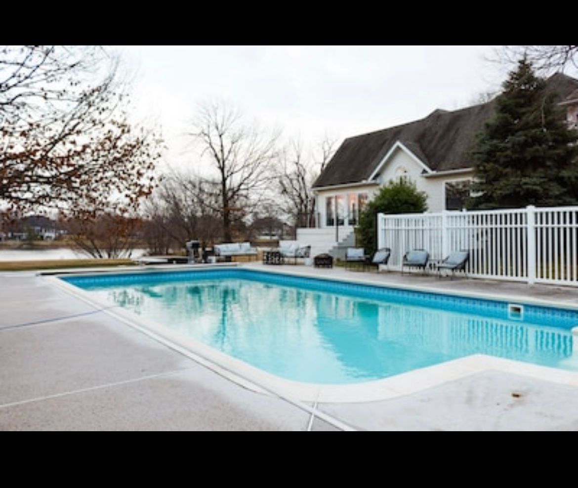 A large swimming pool surrounded by chairs and a white fence