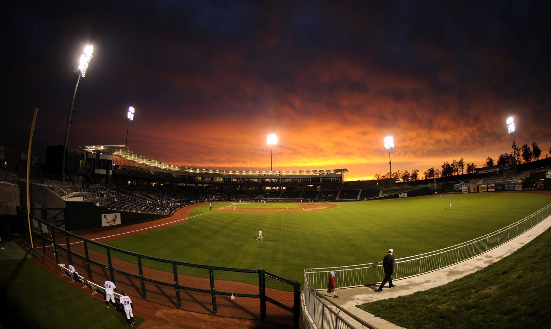 A baseball stadium at night with a sunset in the background.