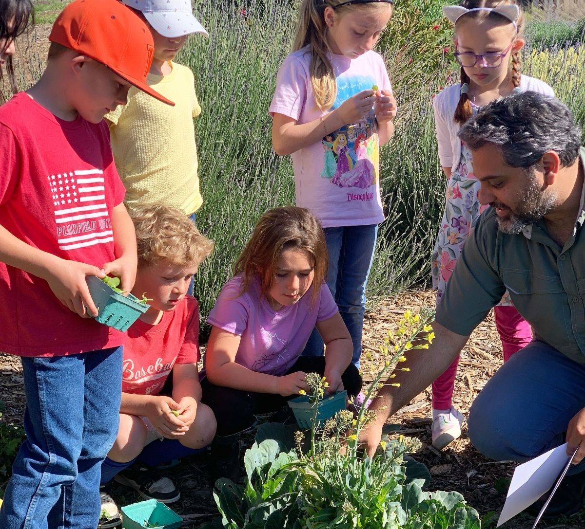 A group of children are gathered around a man in a garden