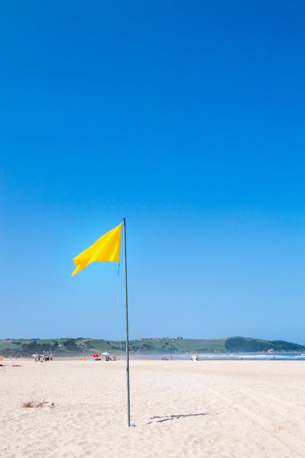 Una bandiera gialla sventola su un palo su una spiaggia.