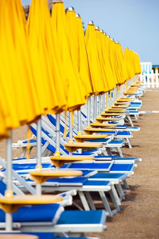 Una fila di sedie blu e ombrelloni gialli su una spiaggia.