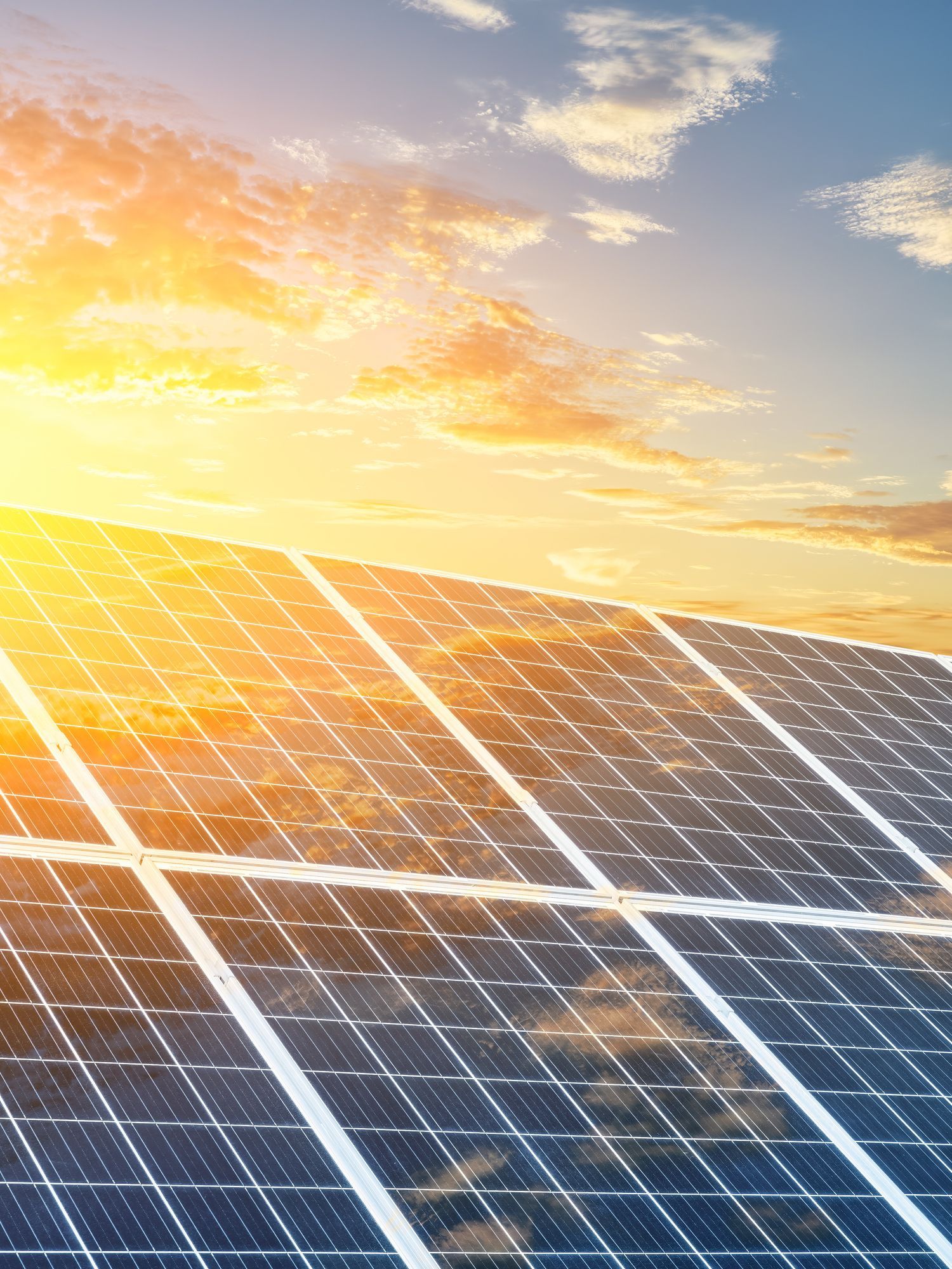 Una fila di pannelli solari contro un cielo al tramonto con il sole che splende attraverso di essi.