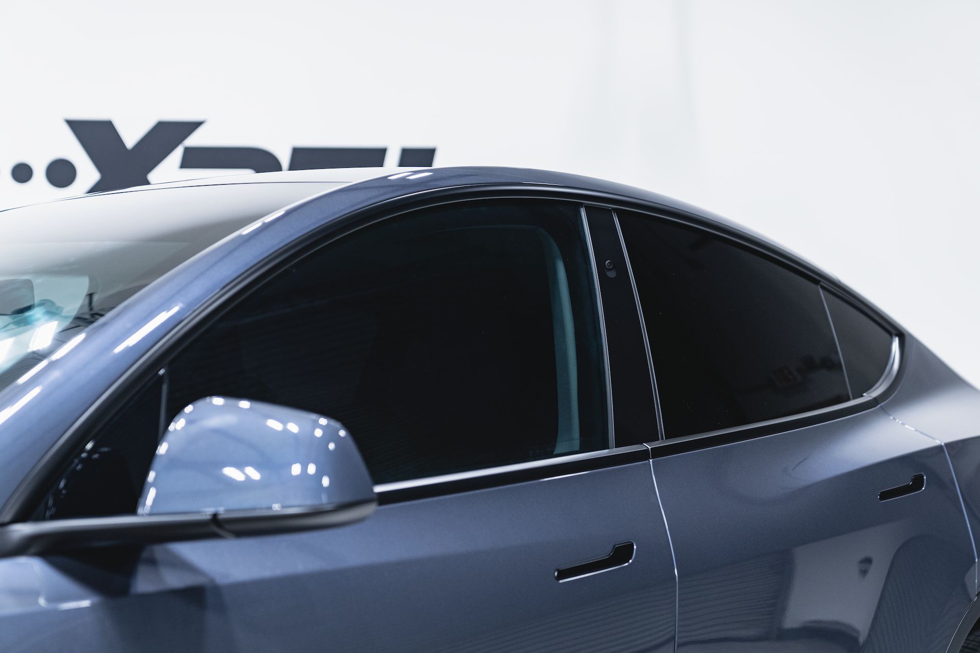 Blue Tesla car with tinted windows, close-up view. Side mirror and door handle visible. White background.