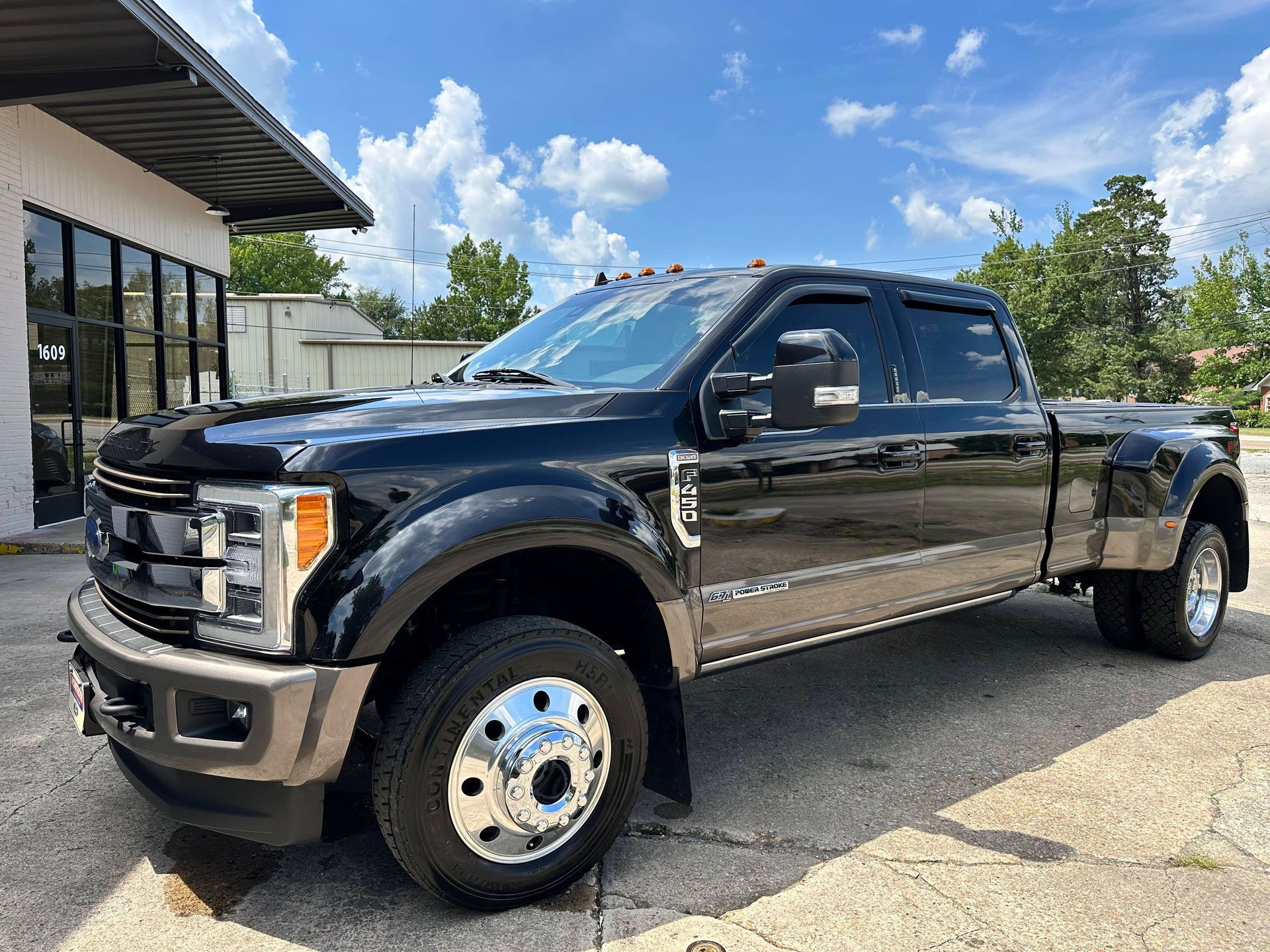 Brown Ford F-350 dually pickup truck parked in front of a building on a sunny day.