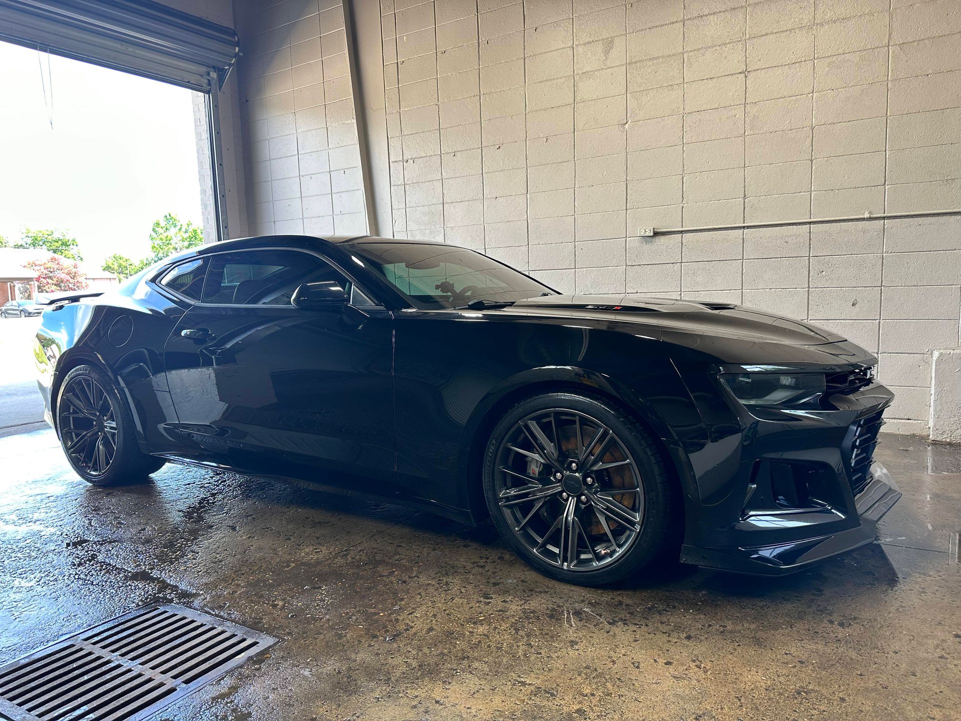 Black Camaro sports car being washed at a car wash bay.