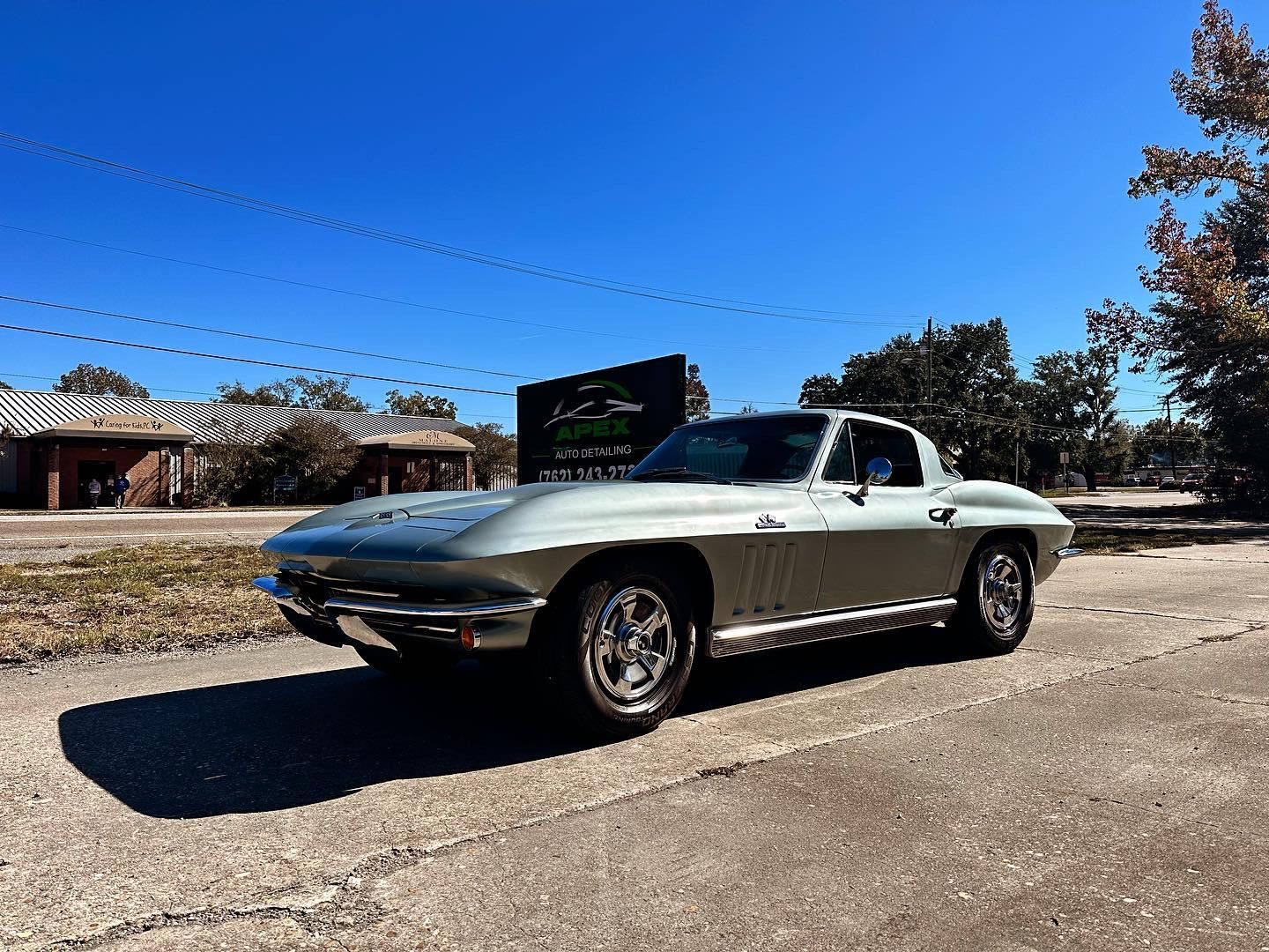 Silver classic Corvette sports car on a sunny street, next to a sign.