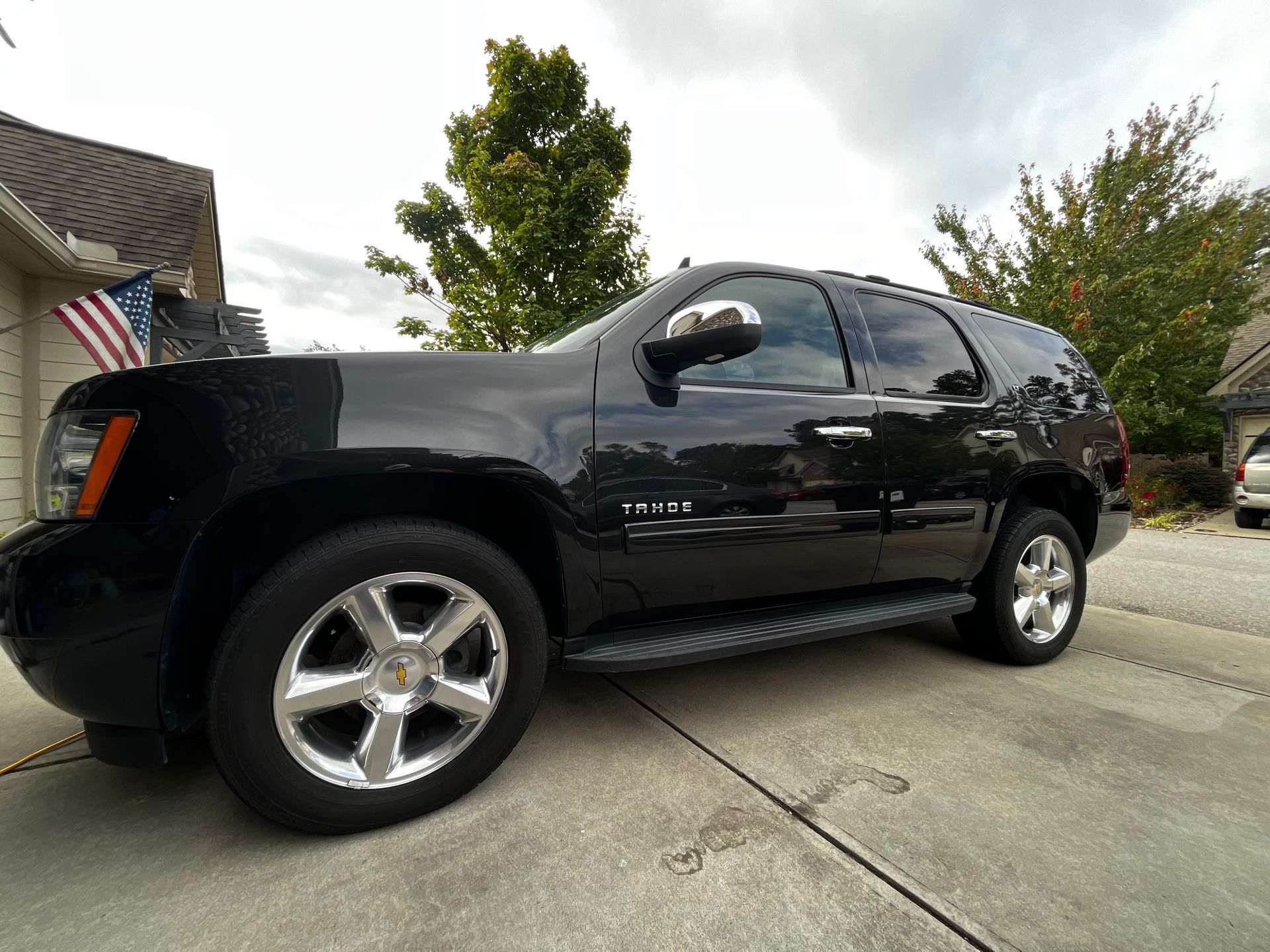 Black Chevrolet Tahoe SUV parked on a concrete driveway in front of a house.