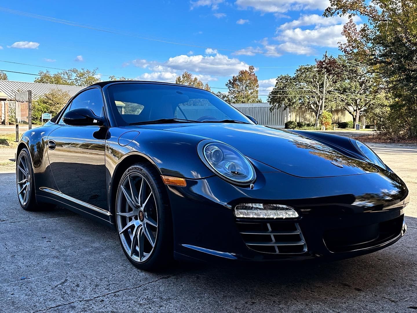 Dark blue Porsche 911 coupe parked on a paved area on a sunny day.