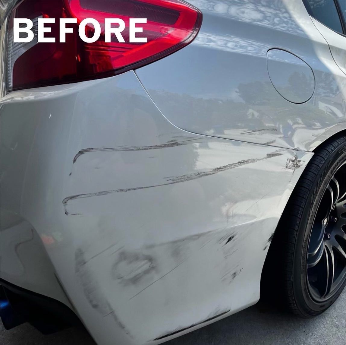 White car's rear bumper before repair, showing multiple scratches and scrapes across the surface.