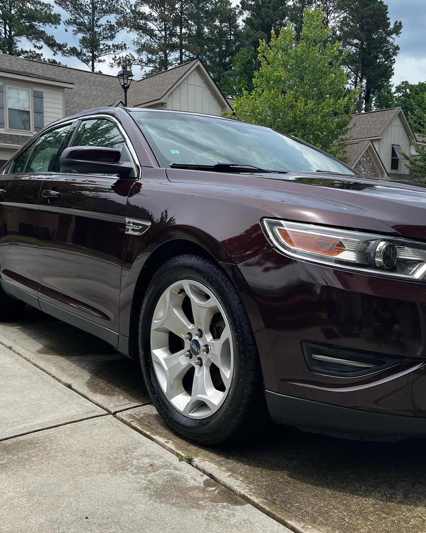 Dark burgundy Ford Taurus sedan parked on a driveway in front of a house.