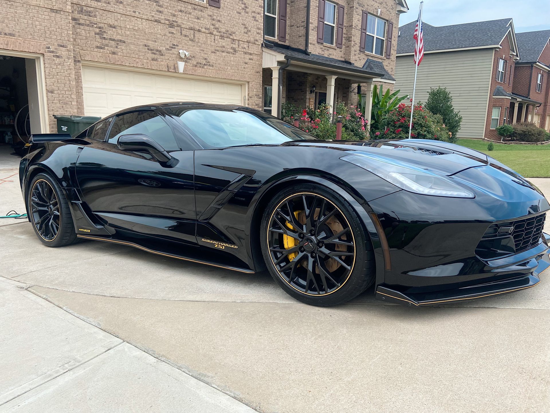 Black Corvette with gold accents parked in front of a house.
