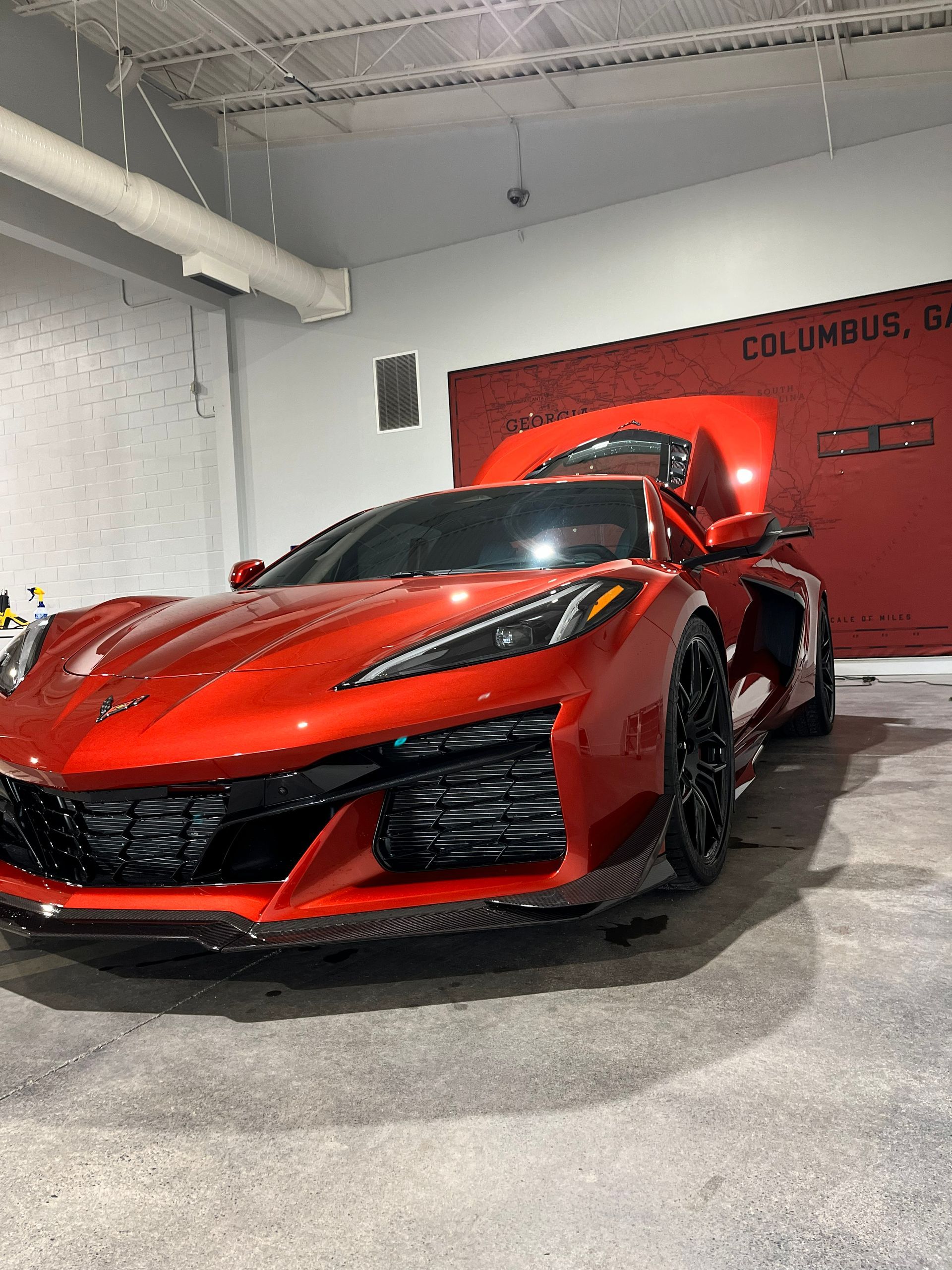 Red sports car, hood open, parked inside a garage.