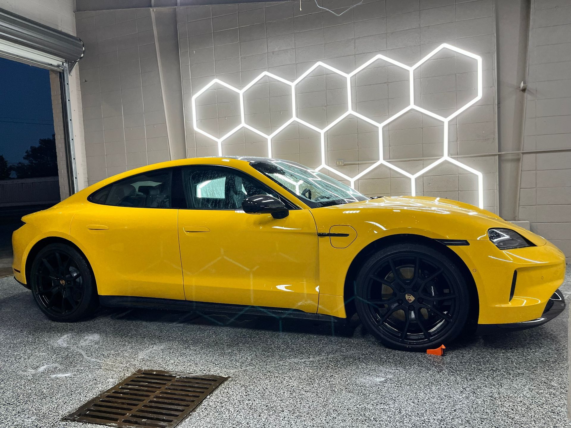 Yellow Porsche Taycan electric car parked inside a garage with honeycomb-shaped lights on the wall.